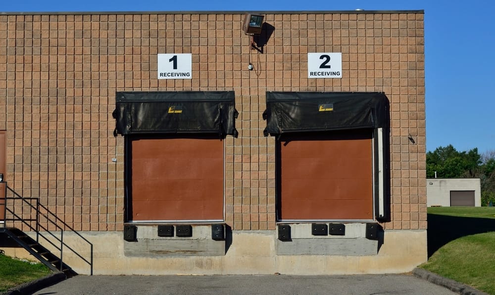 Two dock doors on a brick warehouse wall, signed for receiving.